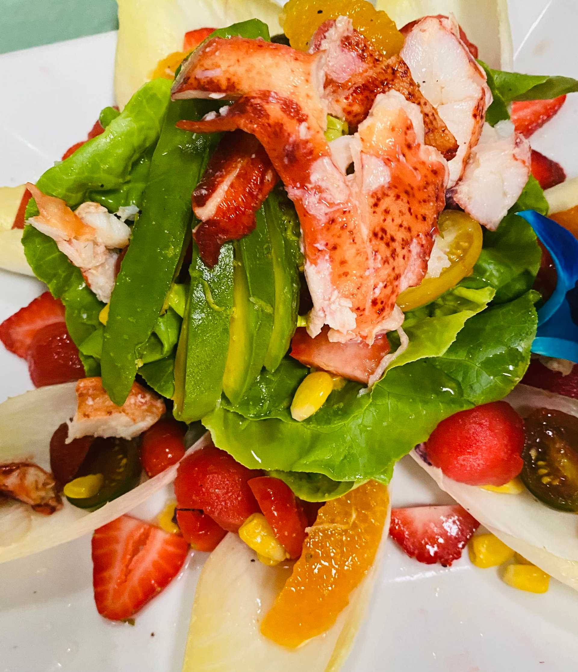 Colorful seafood salad with lobster, avocado, strawberries, and assorted fresh vegetables on a plate.